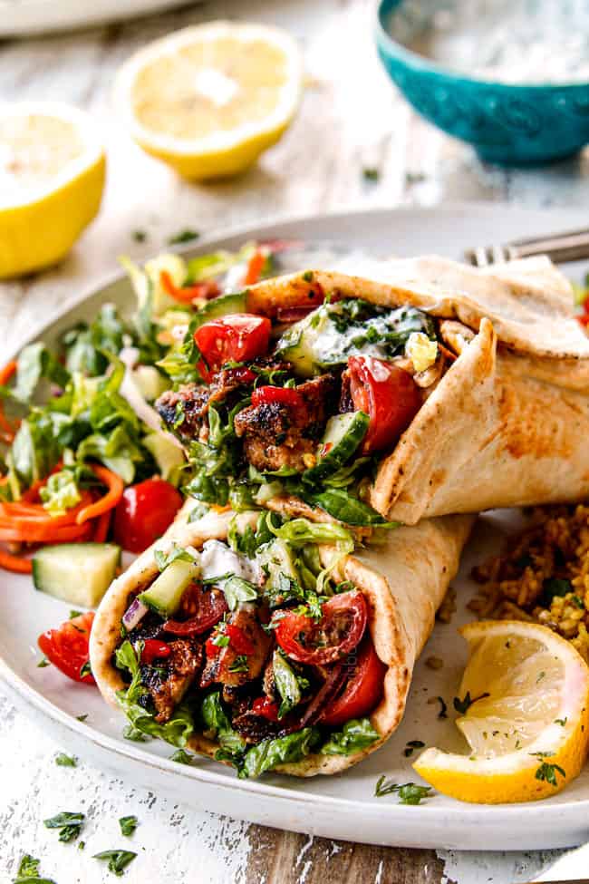 showing how to make doner kebab wraps by adding thinly sliced meat to Lebanese flatbread with hummus, thinly sliced lettuce, thinly sliced red onions, chopped tomatoes, chopped cucumber, chili sauce and garlic yogurt sauce