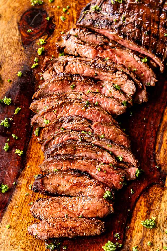 top view of grilled flank steak on a cutting board garnished with parsley