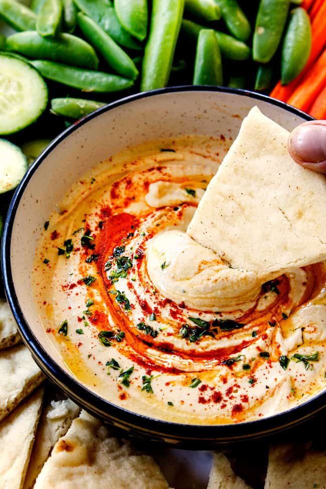 showing how creamy homemade hummus is by dipping pita bread into it