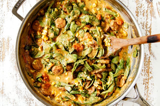 showing how to make spinach pasta recipe by adding spinach and orn to creamy sauce in steel skillet