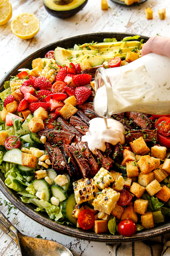 showing how to make steak salad by pouring blue cheese dressing onto the salad