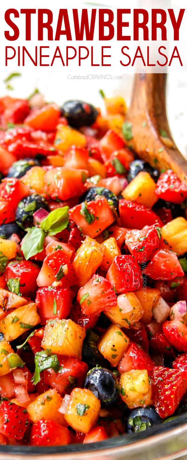 up close showing how to make strawberry salsa by tossing strawberries, pineapples, cilantro, red onions and cilantro together with a wooden spoon