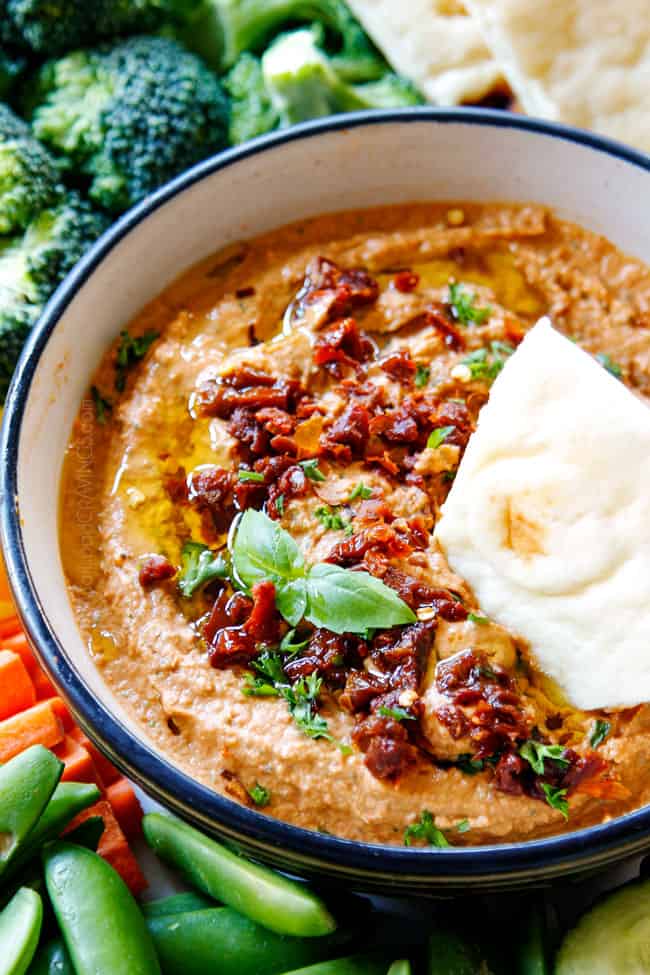 up close sun-dried tomato hummus in a black bowl and a pita wedge