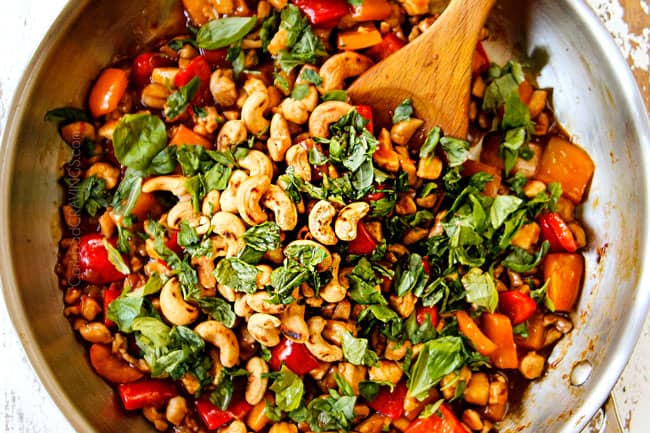 showing how to make Thai basil chicken recipe by adding basil to chicken, bell peppers and sauce in a stainless steel skillet
