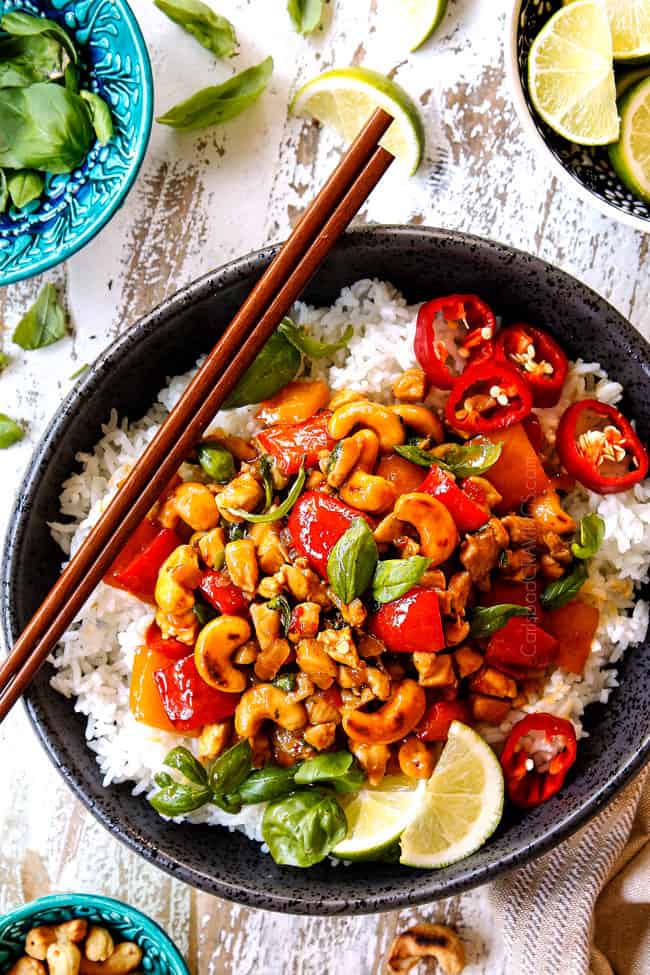 showing how to serve Thai basil Chicken recipe by adding to a bowl of white rice and garnishing with lime wedges and basil