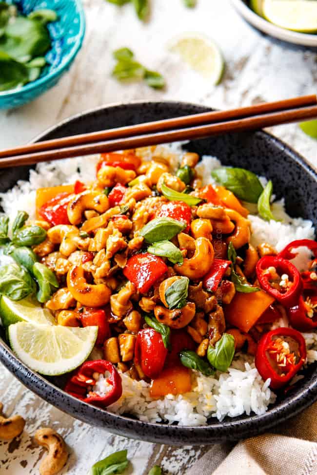 side view showing how to serve basil Chicken by adding to a bowl of white rice in a black bowl with chopsticks