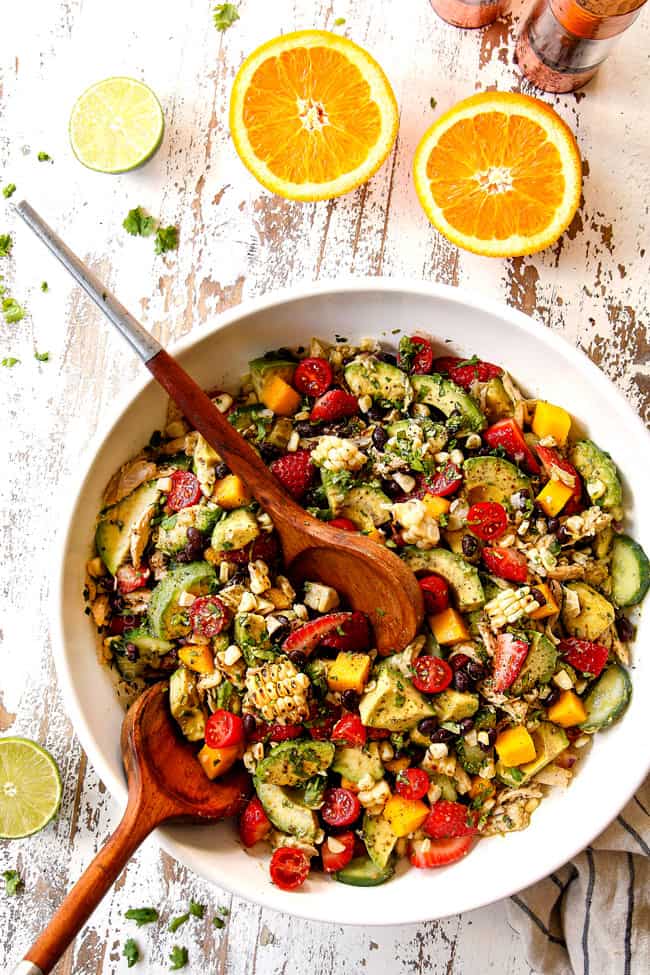 top view showing how to make avocado chicken salad by tossing avocados and vegetables with dressing in a white bowl