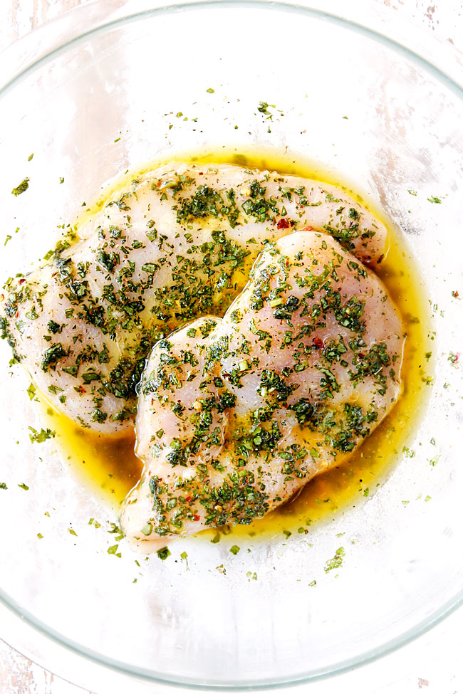 showing how to make grilled chicken salad recipe by marinating chicken breasts in a glass bowl with olive oil, lemon juice, basil and garlic