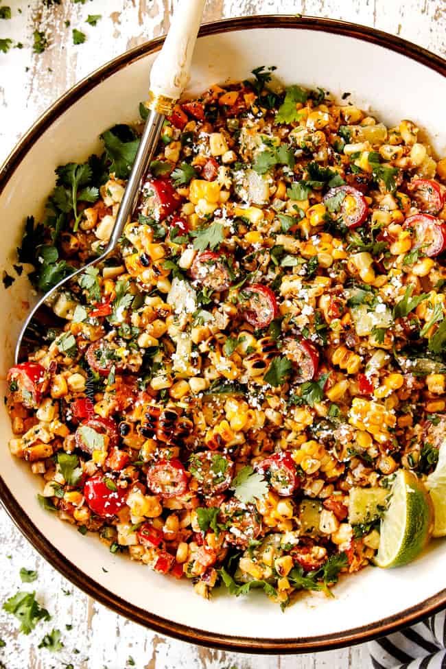 top view of Mexican Street Corn Salad (esquites) in a white bowl with a silver serving spoon