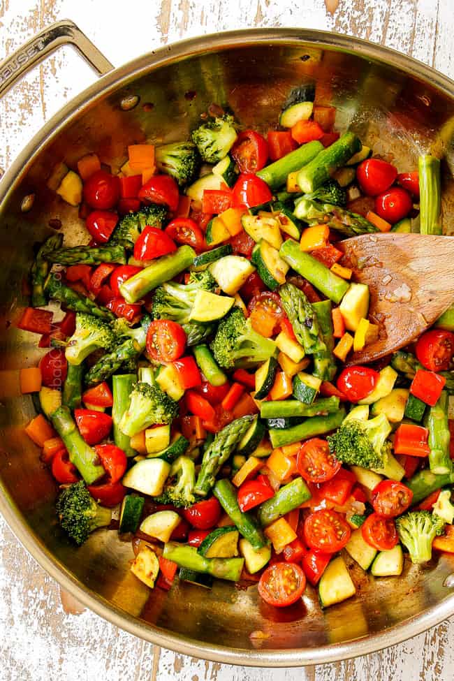 showing how to make pasta primavera by cooking broccoli, bell peppers, asparagus, zucchini and squash in a stainless steal skillet,
