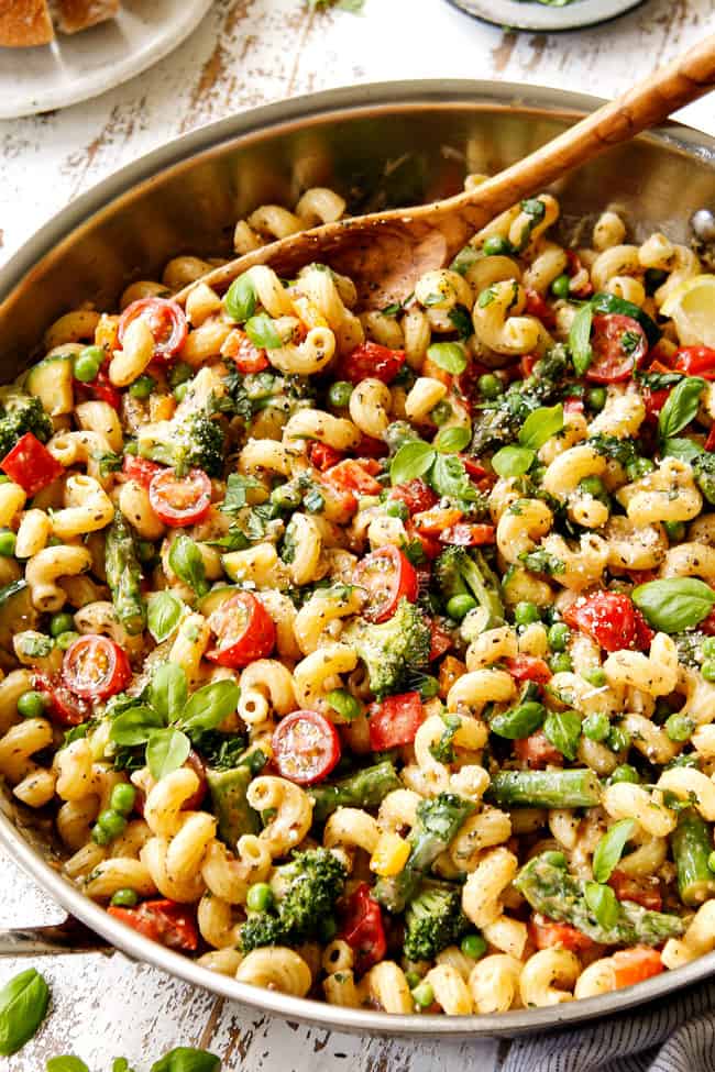 showing how to make pasta primavera recipe by combining pasta, cream sauce and vegetables in a stainless steel skillet and garnishing with Parmesan