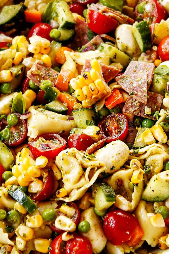 up close of pesto pasta salad with mozzarella, tomatoes and peas in a white bowl