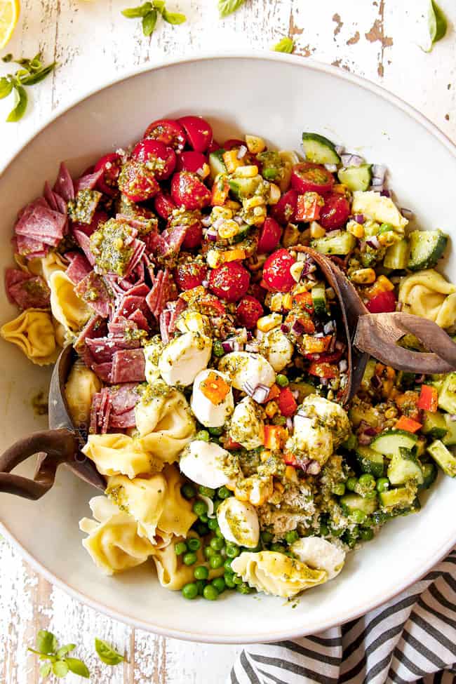top view showing how to make pesto pasta salad recipe by tossing the ingredients with the pesto dressing in a white bowl