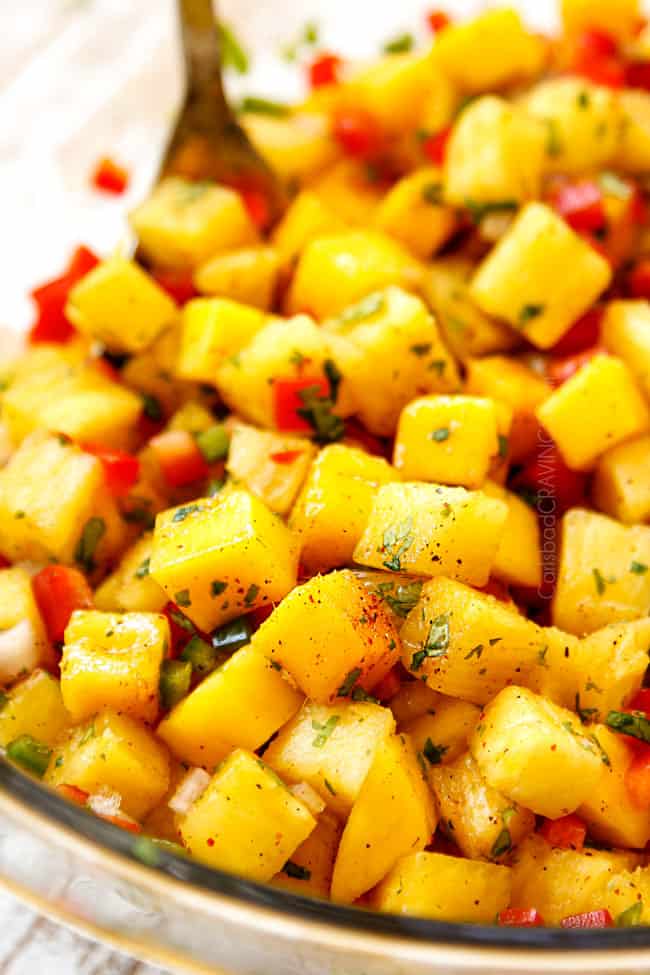 a spoon scooping up top view of pineapple mango salsa in a glass bowl