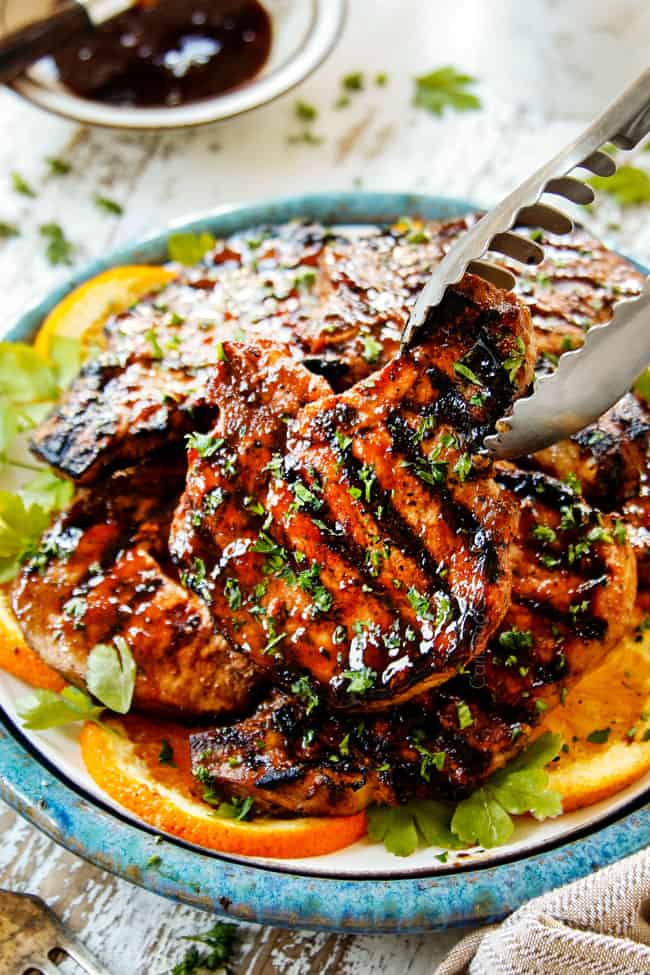 picking up a pork chop with tongs on a plate that has been marinated in best pork chop marinade recipe