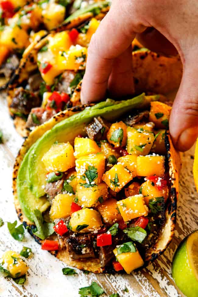 a hand picking up a flank steak taco with chopped flank steak, salsa, avocados and cilantro