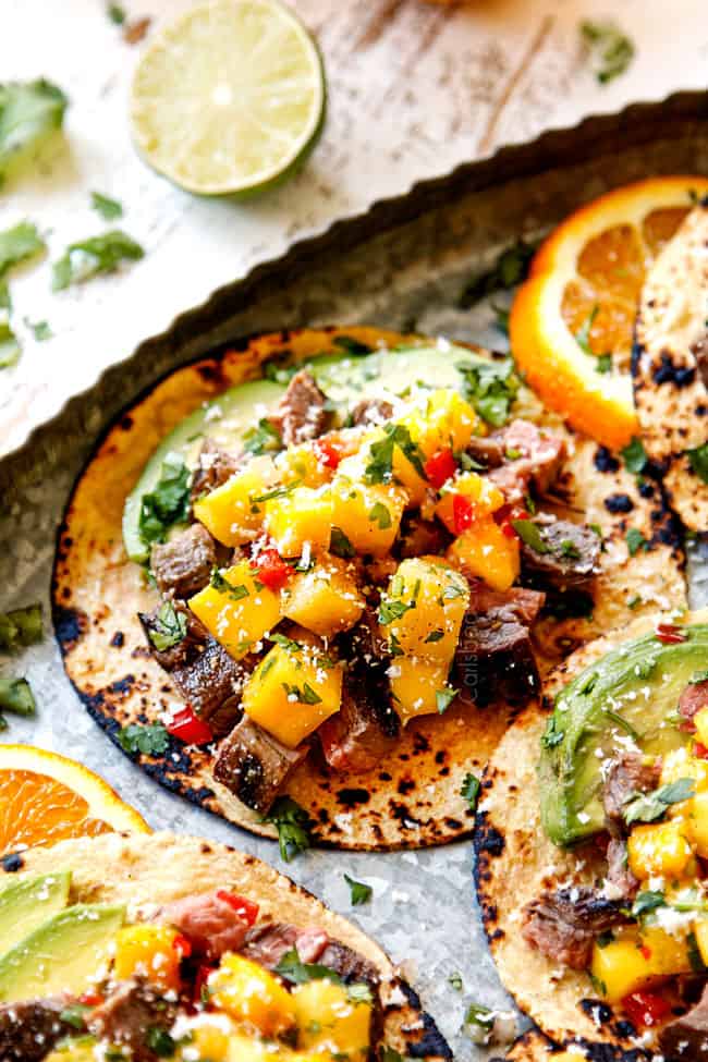 up close of steak taco recipe lined on a metal platter with cilantro and avocado