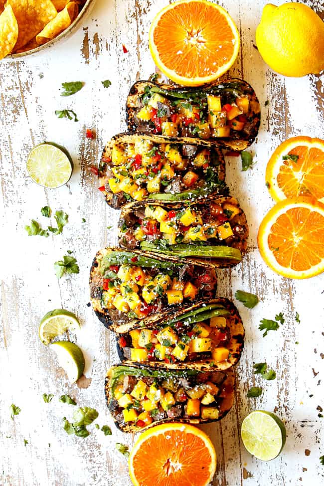 top view of flank steak tacos lined on a white background with salsa
