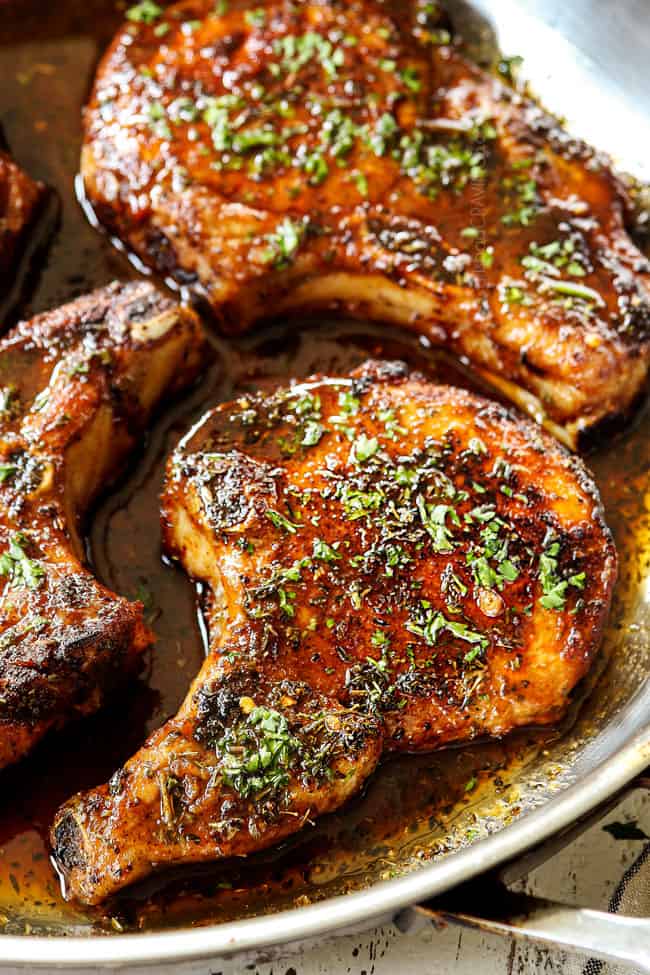 up close of baked pork chops in a brown sugar sauce in a stainless steel skillet