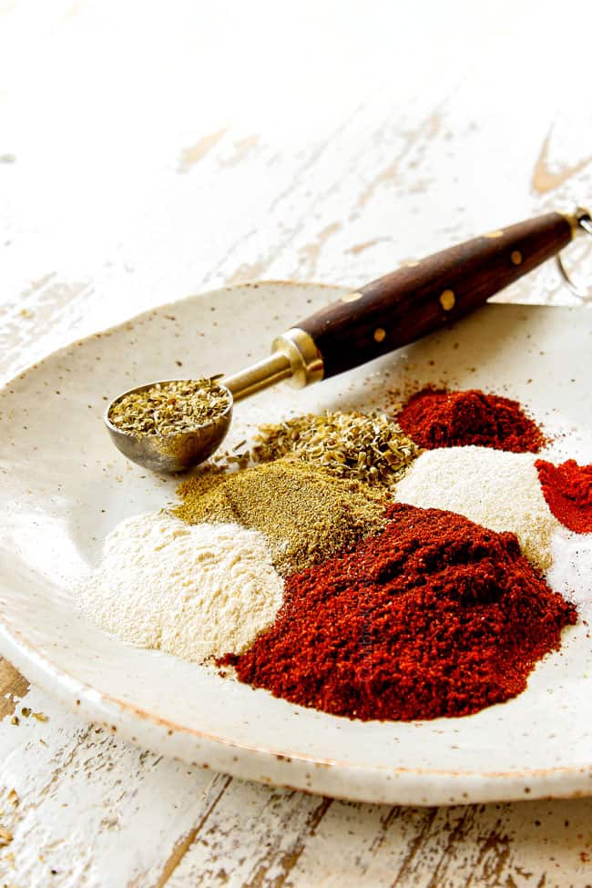 side view of making fajita seasoning recipe by adding chili powder, ground cumin, smoked paprika, garlic powder, onion powder, salt, pepper and cayenne pepper to a tan dish.