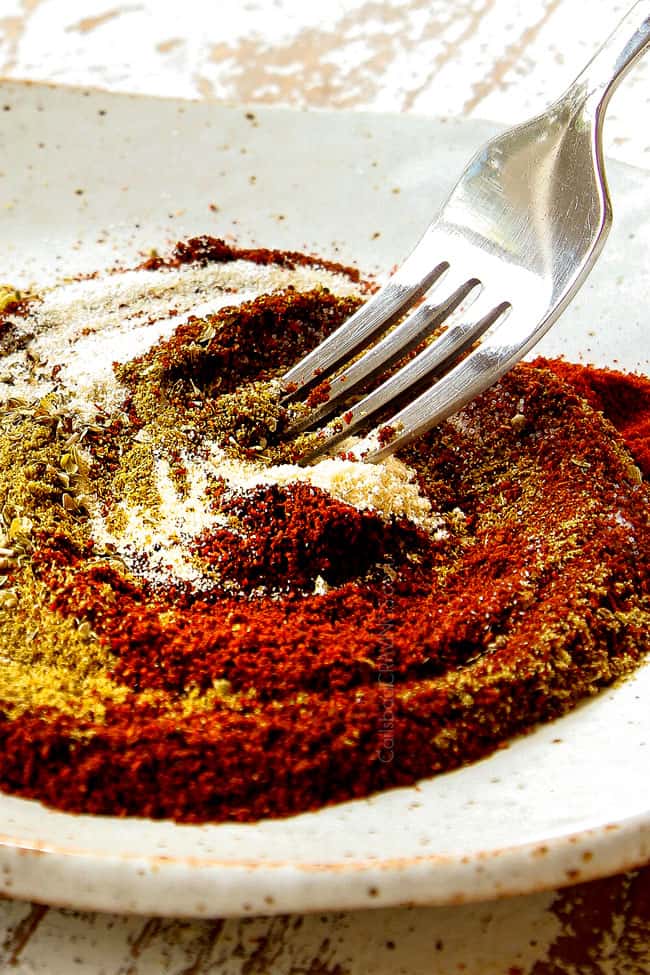 showing how to make homemade fajita seasoning recipe stirring together chili powder, ground cumin, smoked paprika, garlic powder, onion powder, salt, pepper and cayenne pepper to a tan dish with a fork.