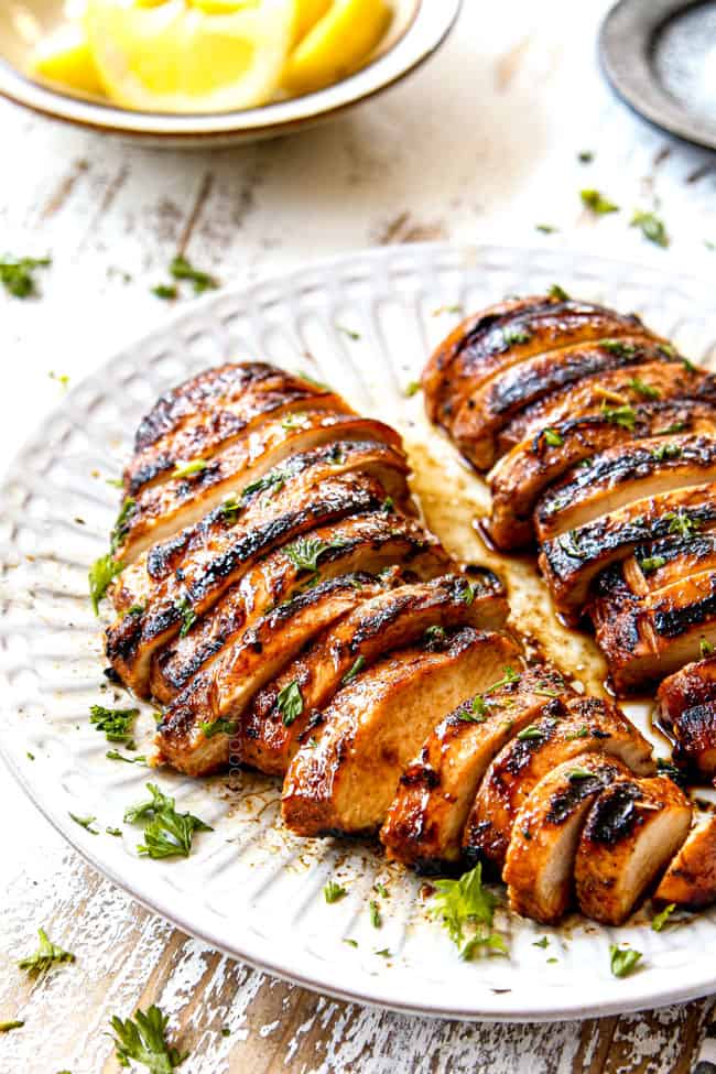 side view of the best marinated grilled chicken on a white plate garnished with parsley