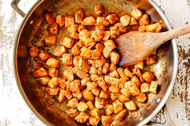 showing how to make mango chicken recipe by cooking chopped chicken breasts with red curry paste in a stainless steel pan