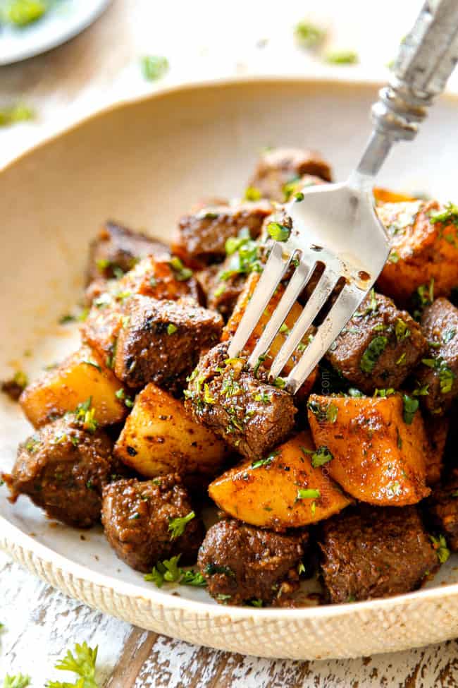 a fork stabbing a steak bite from a tan plate of steak and potatoes