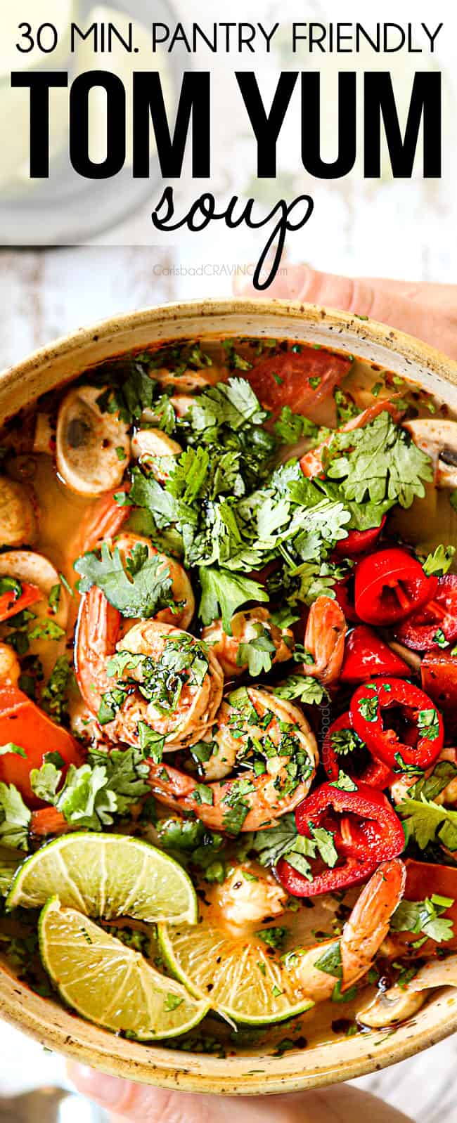 top view of two hands holding bowl of Tom Yum Soup with shrimp