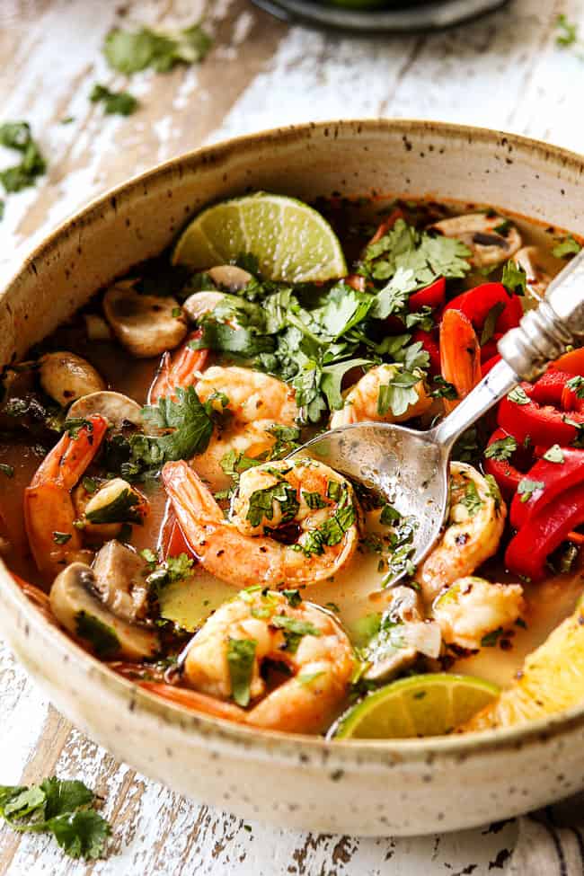 up close of a bowl of Tom Yum Soup recipe with a spoon scooping up shrimp