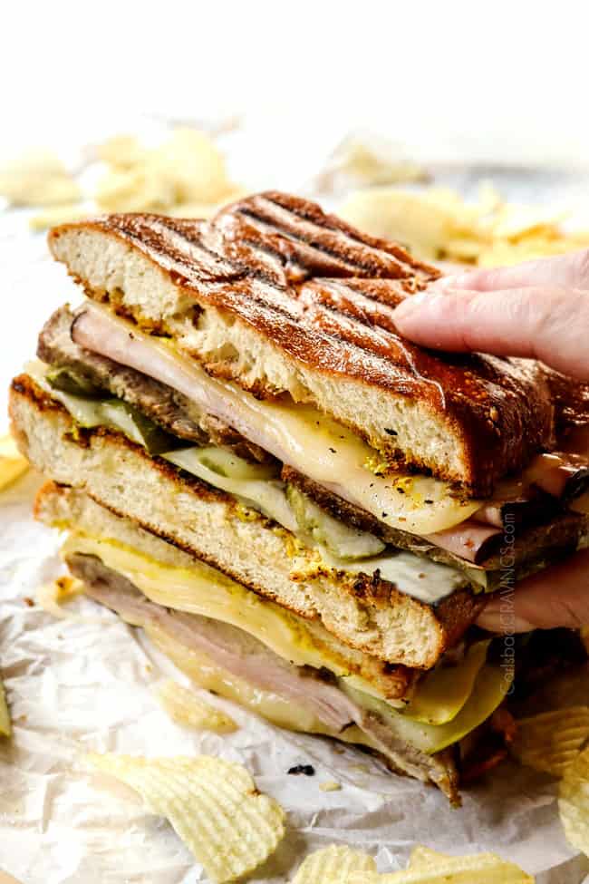 a hand picking up a Cubano sandwich (Cubano) with Swiss cheese, mojo pork, ham, pickles and mustard