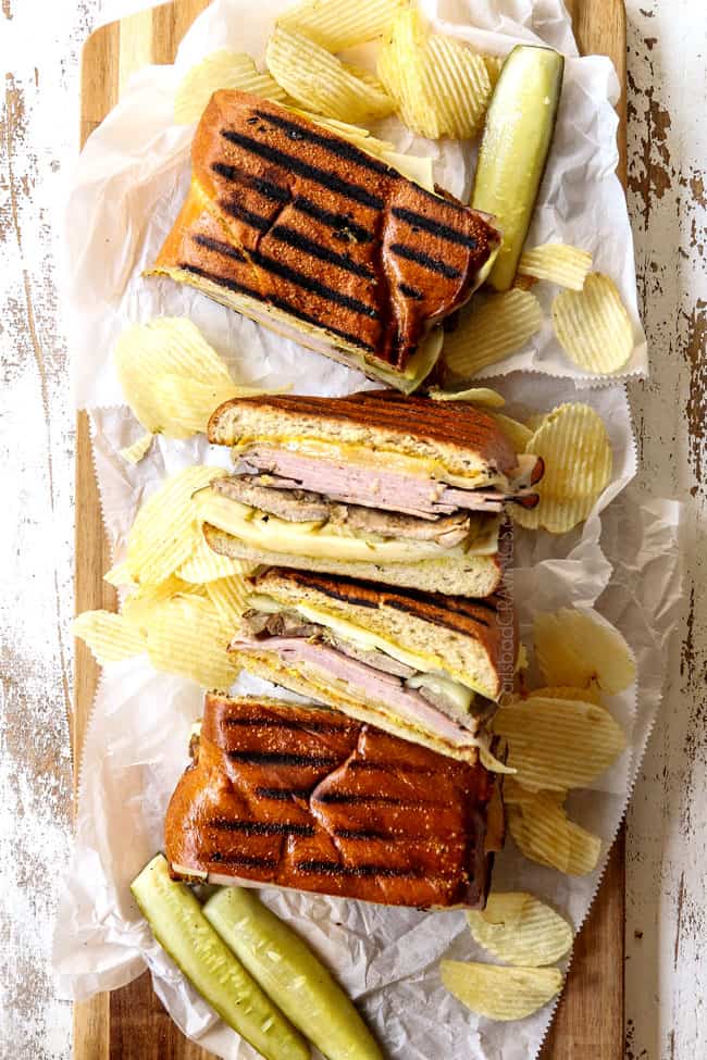 four Cubano sandwiches (Cubanos) on a a wood platter surrounded by potato chips