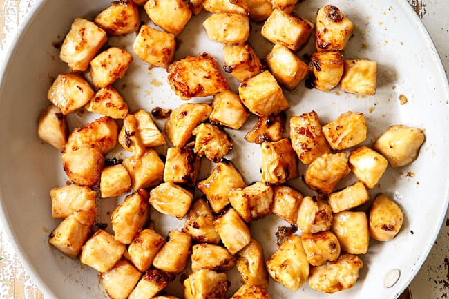 showing how to make kung pao chicken by cooking chicken in a white skillet