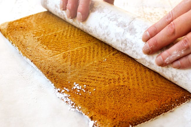 showing how to make a pumpkin roll by rolling up the cake with parchment paper
