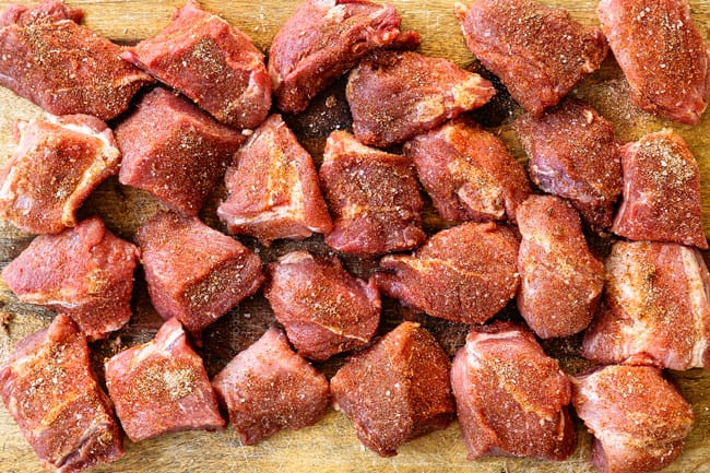 showing how to make pozole by seasoning chunks of pork on a cutting board