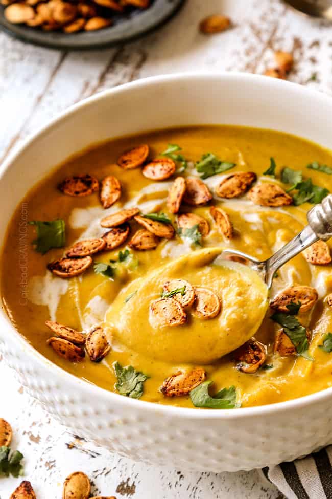 a spoon scooping up creamy pumpkin soup in a white bowl