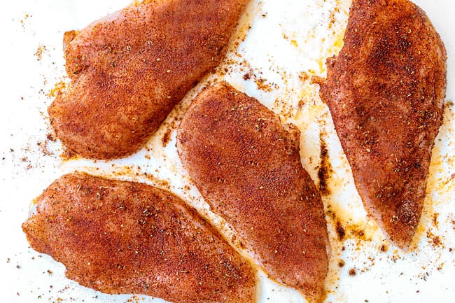 showing how to make salsa chicken recipe by rubbing chicken on white cutting board with a spice rub