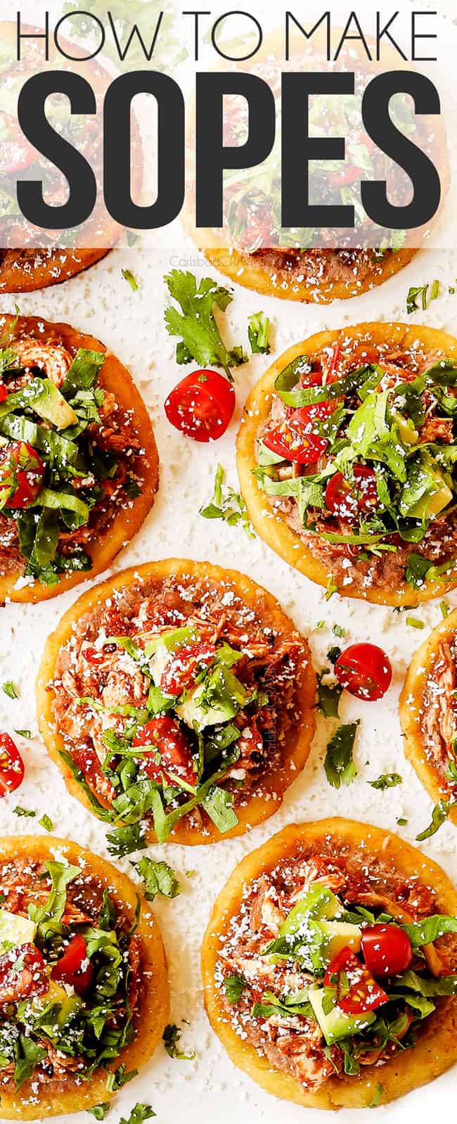 top view of sopes on a white platter topped with refried beans, shredded chicken, lettuce, tomatoes and avocados