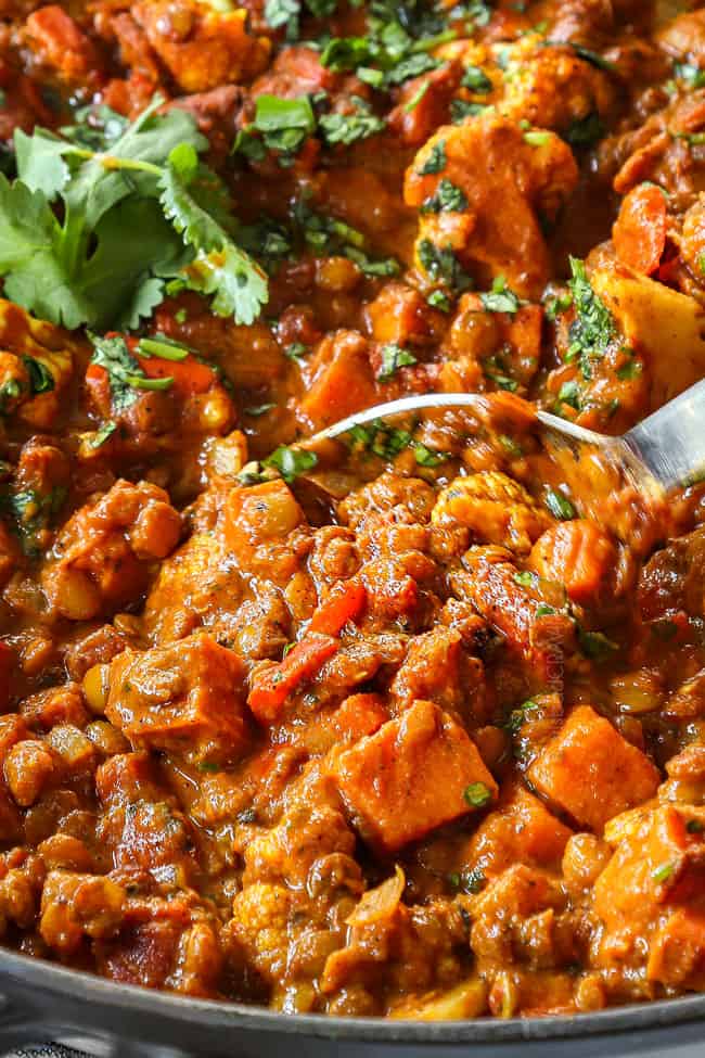 side view of lentil curry in a black pot with a spoon showing how creamy it is