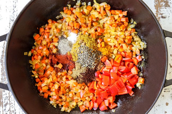 showing how to make lentil curry recipe by adding yellow curry, garlic, ginger, turmeric, coriander, cayenne pepper, cumin to a black pot to bloom the spices