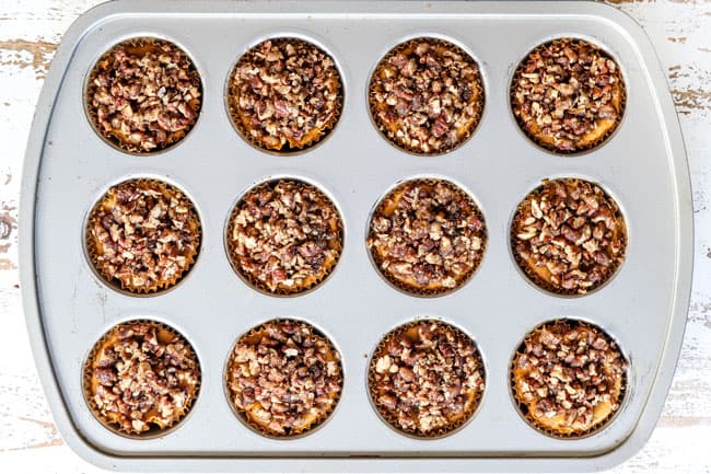 process shot showing how to make mini pumpkin cheesecakes by adding pecan praline topping to mini cheesecakes