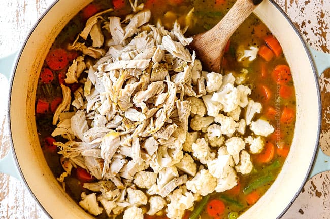 showing how to make leftover turkey rice soup by adding leftover turkey and cauliflower to a white Dutch oven
