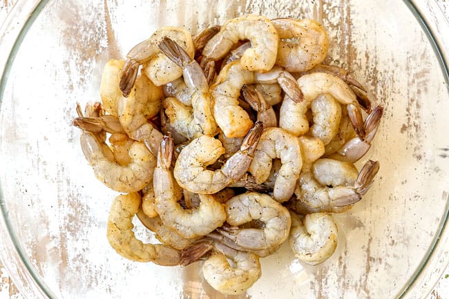 showing how to make shrimp stir fry recipe by adding raw shrimp to a glass bowl and marinating with soy sauce and rice wine