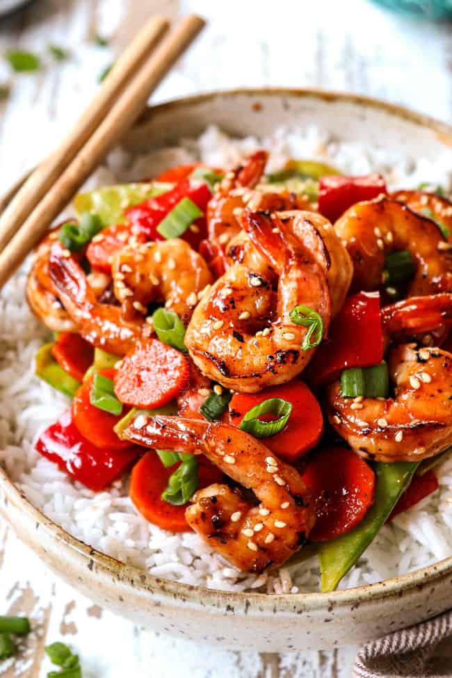 up close of shrimp stir fry with white rice in a bowl garnished with green onions