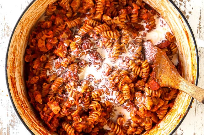 showing how to make Chicken Parmesan Pasta by stirring in heavy cream