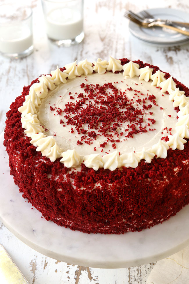 red velvet cheesecake recipe on a white pedestal decorated with red velvet crumbs