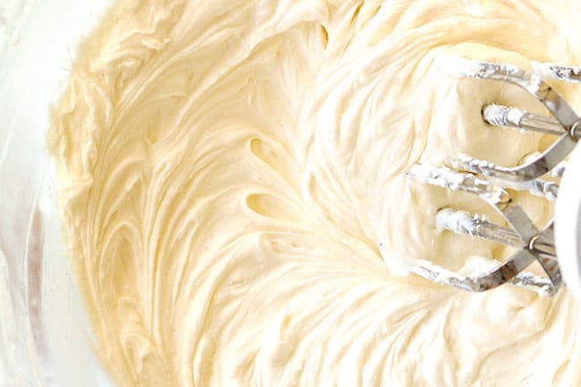 showing how to make red velvet cheesecake by creaming butter, sugar and cream cheese together until smooth