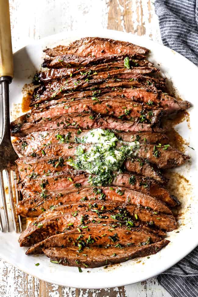 top view of London Broil on a white platter with herb butter