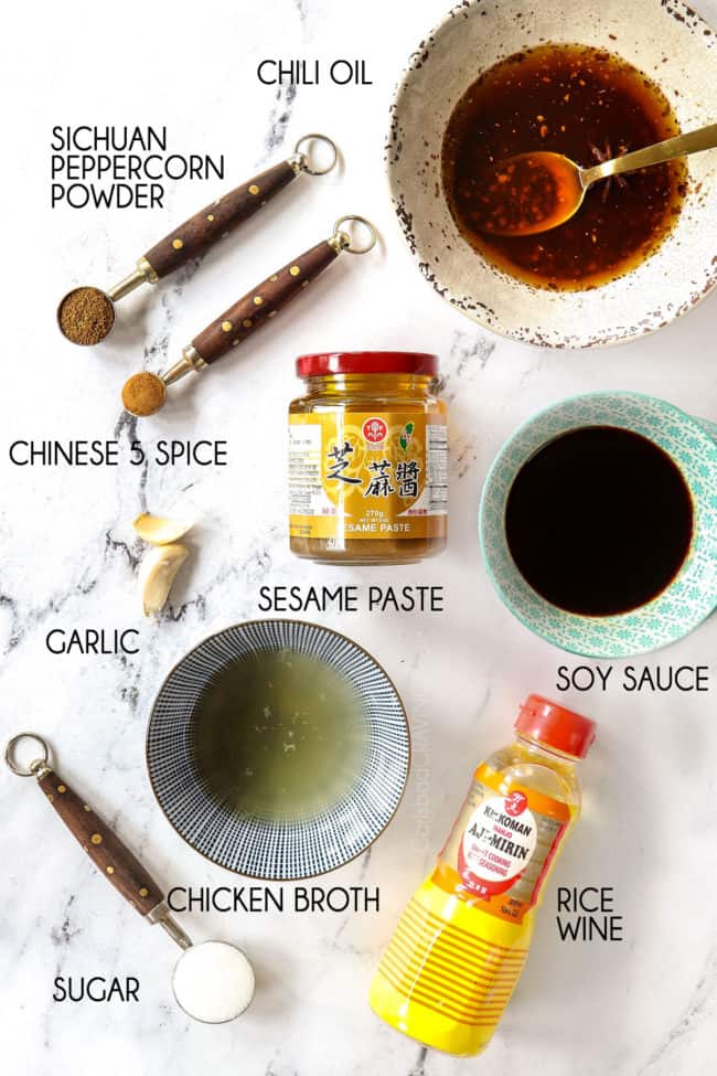 showing how to make Dan Dan Noodles recipe by lining up Dan Dan Sauce ingredients: Chinese sesame paste, chili oil, rice wine, soy sauce, chicken broth, Chinese 5 spice, sugar, chili oil, Sichuan peppercorns