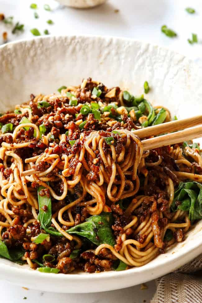 Dan Dan Noodles in a white bowl with pork, choy yum, green onions